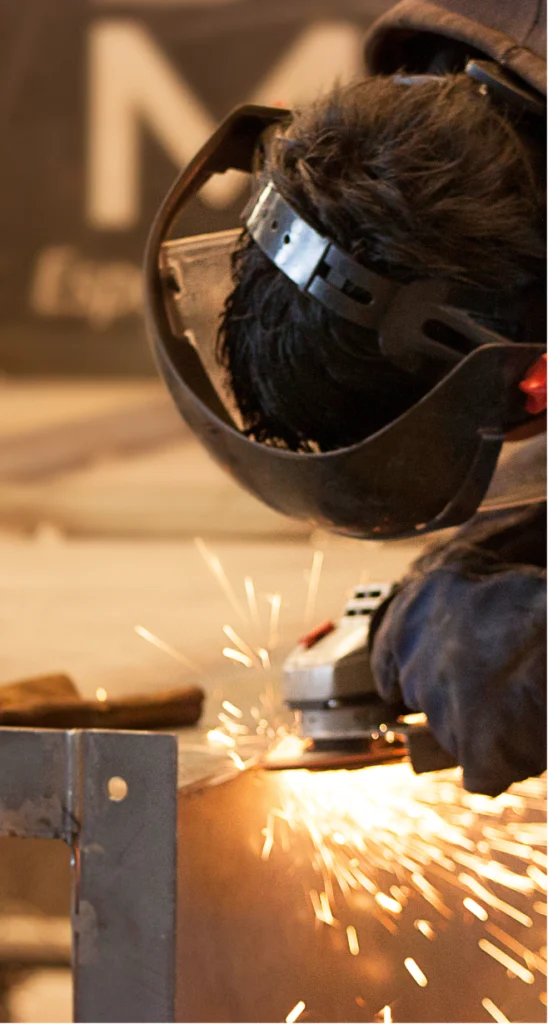 Operario de MCAT realizando trabajo de soldadura y esmerilado en estructuras metálicas industriales.