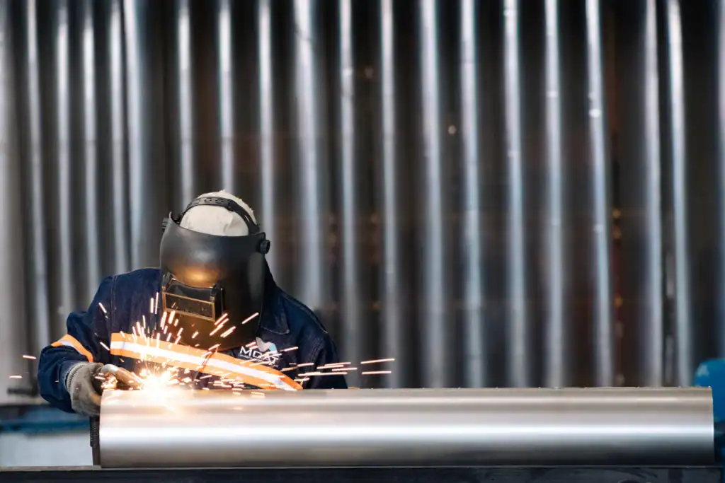Soldador de MCAT fabricando ducto industrial con equipo de protección y chispas de soldadura