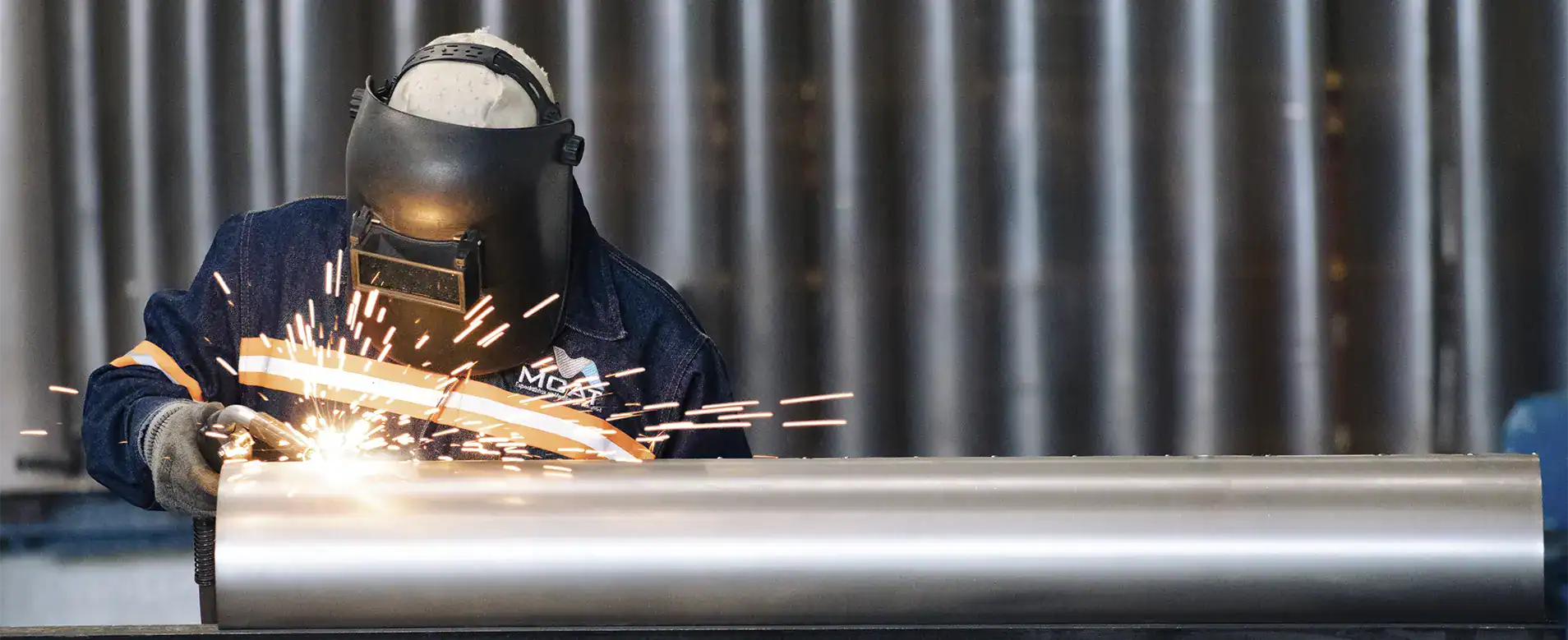 Soldador de MCAT fabricando ducto industrial con equipo de protección y chispas de soldadura
